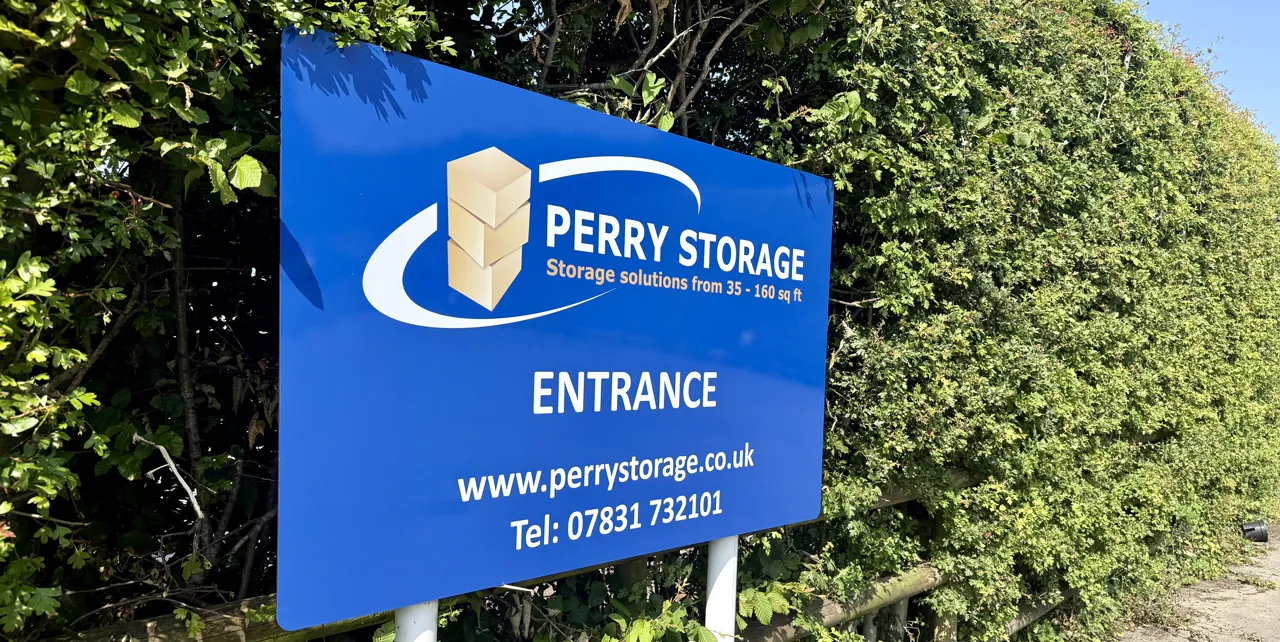 The blue Perry Storage entrance sign among green hedging